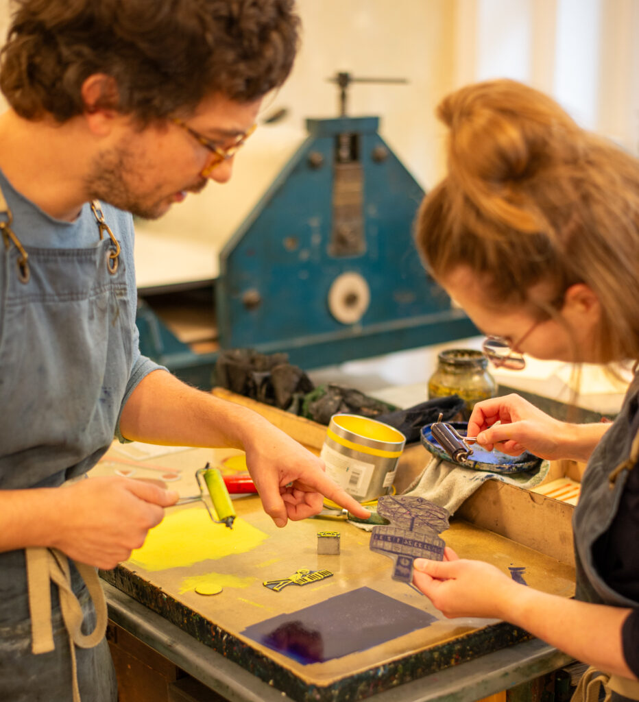 Alberto und Anja drucken ein Klischee, das die Weltzeituhr abbildet. Sie sind gerade dabei die Druckplatte einzufärben.